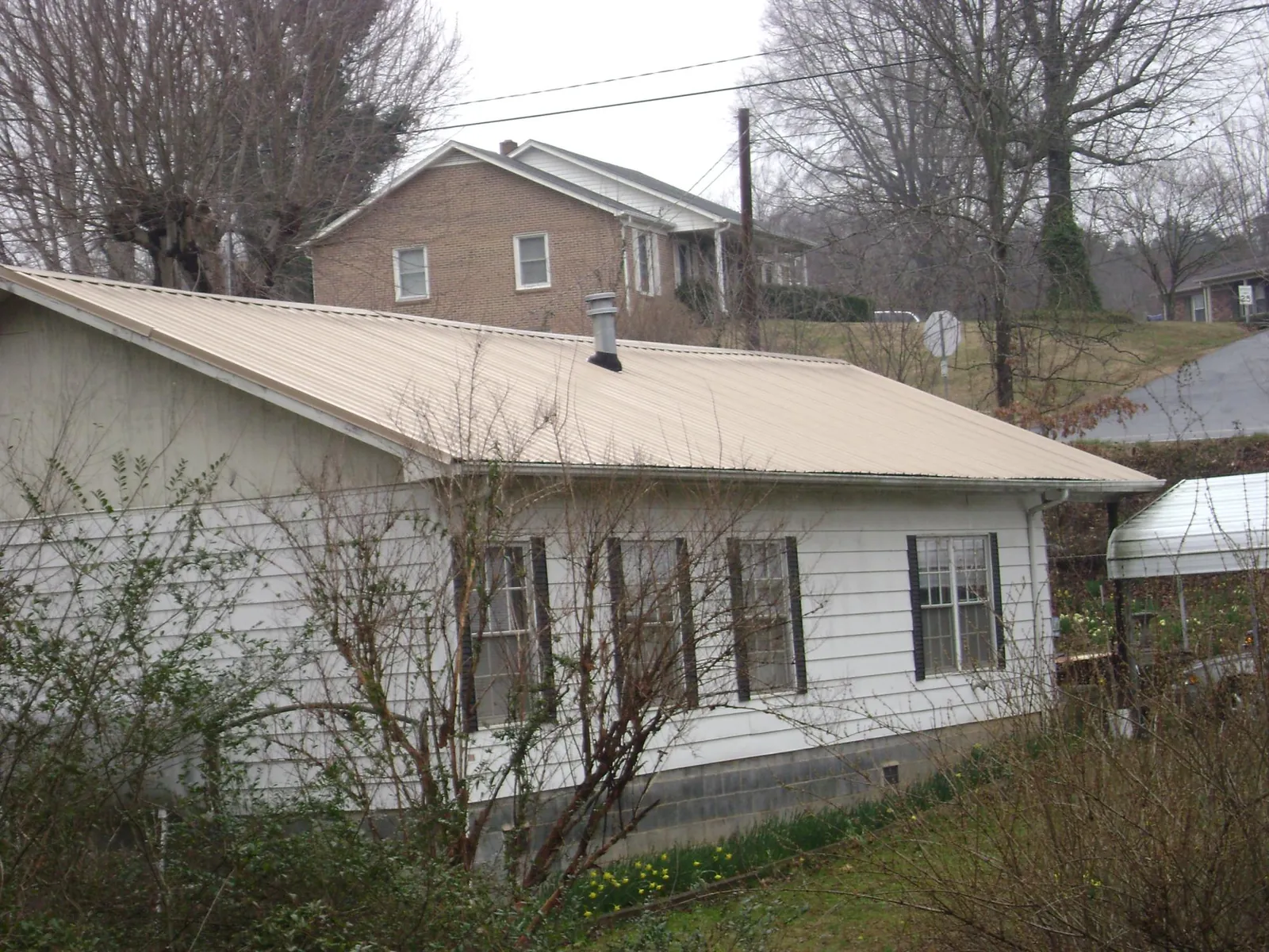 Tan metal roof on a white sided house set into a hillside — Commercial Roofing by Roofing Brothers in Nottingham